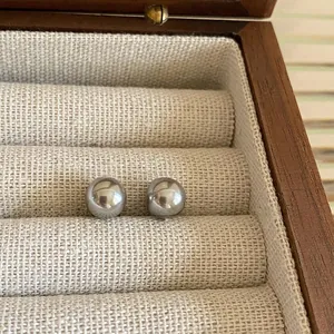 Macro shot of dark grey round pearl earrings on beige linen inside a wooden box
