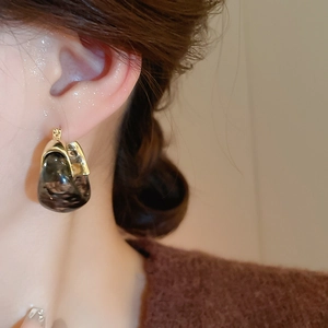 Close-up of U-shaped tortoiseshell resin earring with gold frame worn with brown knitwear