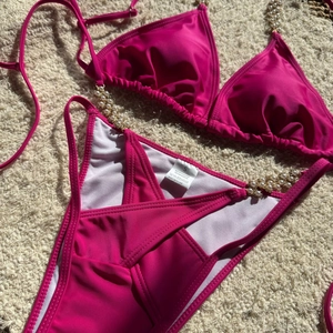 Detail of fuchsia bikini featuring white pearls and gold beads on a soft plush background