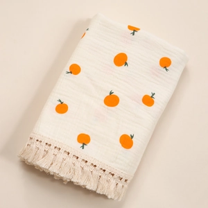 Close-up of cotton baby swaddle with orange prints and tassel fringe detail