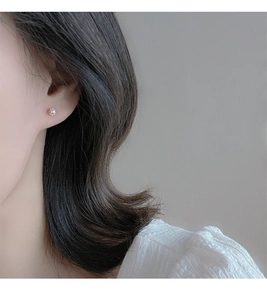 Close-up of minimalist pearl stud earring with gold screw back on a woman's earlobe