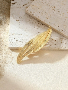 Close-up of golden vintage feather hair clip with detailed metallic texture on stone background