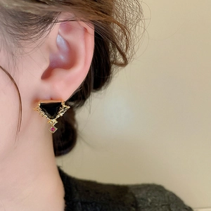 Détail d'une boucle d'oreille triangle dorée avec zircon noir et rouge portée à l'oreille