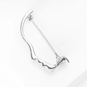 Macro shot of silver abstract face brooch with polished finish and metal pin clasp