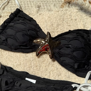 Macro detail of black mesh bikini top featuring a gold starfish charm on textured towel