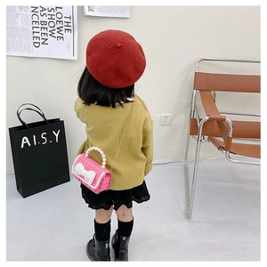 Pink tweed crossbody bag for girls with pearl handle and bow, shown on child model