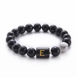 Close-up of 10mm black onyx beads with a white turquoise stone and golden letter E bead
