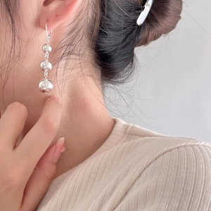 Macro shot of silver triple-sphere drop earrings on a model showing the metallic mirror finish