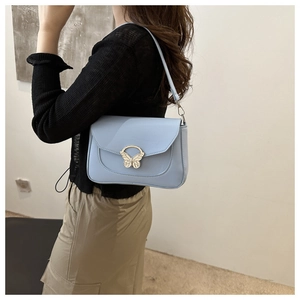 Detail shot of light blue shoulder bag featuring a decorative butterfly buckle on the flap