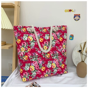 Red canvas tote bag with rose floral print and beige braided rope handles in a cozy setting