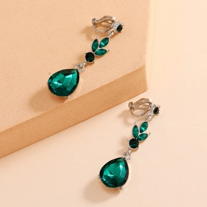 Close-up of teardrop green gemstone ear clips with silver settings on a beige block