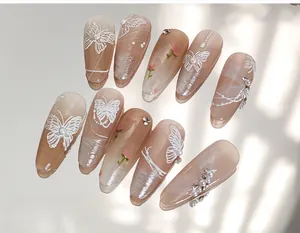 Détail de faux ongles avec papillons blancs, perles et motifs floraux de couleur abricot