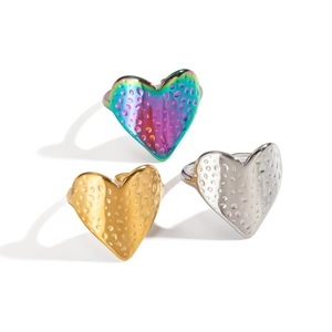 Trois bagues coeur texturées en finitions arc-en-ciel, or et argent sur fond blanc