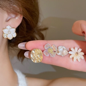 Detailed close-up of floral stud earrings set including white camellia and golden rose designs