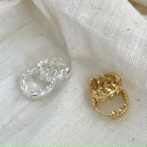 Détail des créoles feuilles en or et argent d'inspiration naturelle sur lin blanc