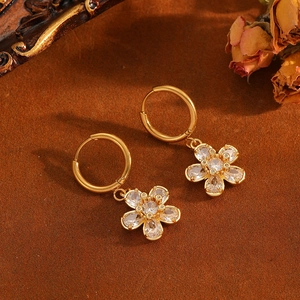 Gros plan de créoles dorées avec pendentifs fleurs en zircone étincelante sur fond vintage
