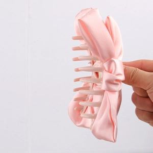 Detail of pink satin fabric bow hair claw clip showing shark clip teeth structure
