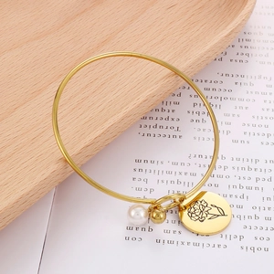 Detailaufnahme des goldenen Geburtsblumen-Armreifs mit Perle und eingraviertem Anhänger