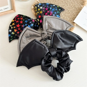 Three Halloween bat wing hair scrunchies in black satin, silver, and star patterns