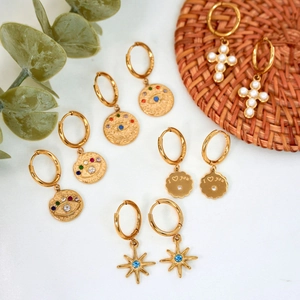 Gold hoop earrings with evil eye, star, heart, and pearl cross charms on white fabric