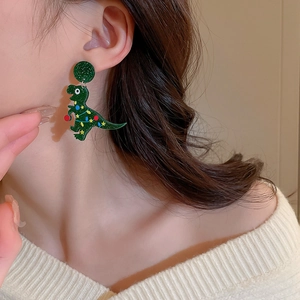Close-up of glittery green Christmas dinosaur earrings worn by a model in a cozy setting