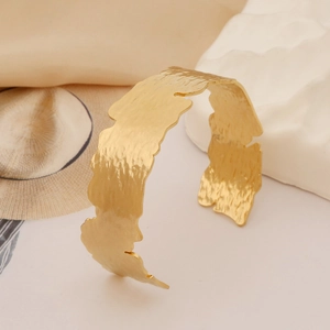 Detail of gold open cuff bangle with hammered texture on minimalist white pedestal