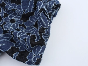 Détail macro de broderie florale bleue sur tulle noir avec texture de denim