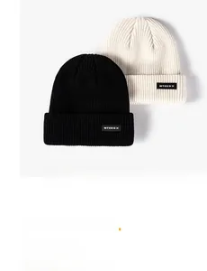 Detail of ribbed knit beanies in black and beige with stitched MTEESX brand label