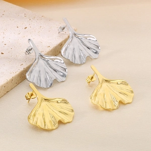 Close-up of wavy ginkgo leaf earrings in gold and silver finish on soft fabric