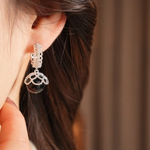Detail of silver drop earring with black bead and hollow floral metalwork on a model