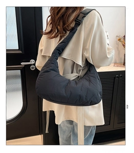 Détail de la texture matelassée du sac noir avec bandoulière large en tissu réglable