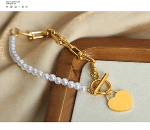 Close-up of pearl bead and gold U-link chain bracelet with heart charm and OT clasp