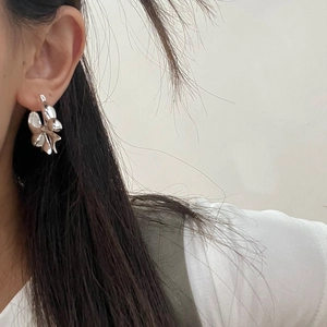 Detail view of silver bow-shaped earrings on a model showing high-gloss metallic finish