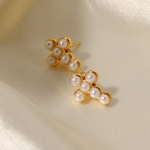 Detailed view of gold-plated cross stud earrings with six white pearls on silk fabric
