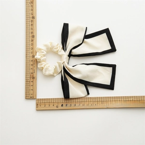 Elegant cream satin bow scrunchie with black piping edges for classic hair styling