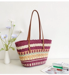 Detail of colorful striped woven straw tote bag with brown handles on a styled table