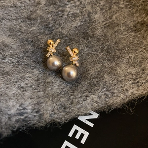 Detailed close-up of a pearl drop earring with gold knot and zircon on knit fabric