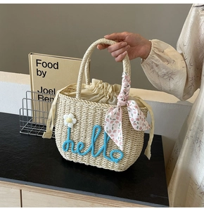 Detail of straw woven handbag featuring blue hello embroidery and floral silk scarf accessory