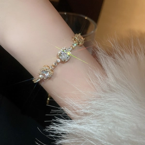 Détail du bracelet plaqué or avec trois zircons carrés sur une manche en fourrure blanche