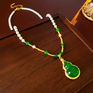 Détail du pendentif gourde vert émeraude et collier de perles sur plateau en bois