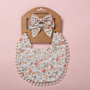 Détail d'un bavoir bébé bohème à fleurs avec pompons et son bandeau nœud assorti