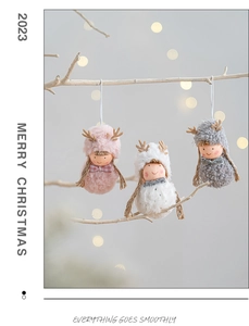 Detail of plush Christmas elk and angel ornaments hanging on white branches with bokeh lights