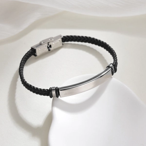 Schwarzes geflochtenes Lederarmband mit silberner Metallstange auf Keramikschale
