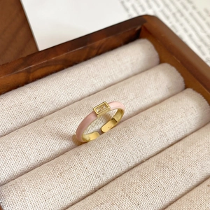 Detail of gold open ring with pink enamel inlay and rectangular zircon in a wooden box