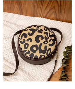 Detail of leopard print round crossbody bag with gold hardware on a cozy knit blanket