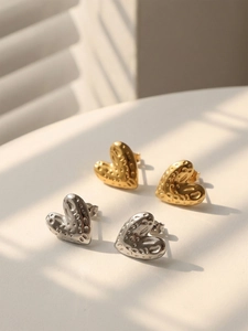 Close-up of heart-shaped gold and silver earrings with hammered metal texture