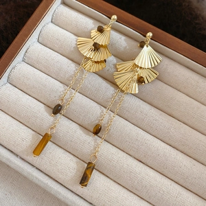 Macro shot of gold ginkgo leaf earrings with tiger eye stone and long metal tassels
