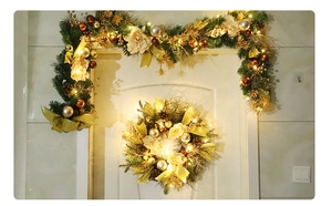 Detailed close-up of a lit Christmas wreath with gold ornaments on a white front door