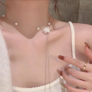 Vue détaillée d'un collier à pompons en perles sur modèle avec pendentif fleur argentée