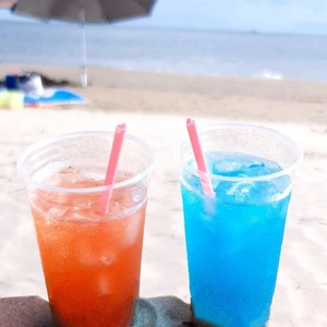 Vista detallada de pajitas rosas en forma de corazón en vasos en la playa de verano.